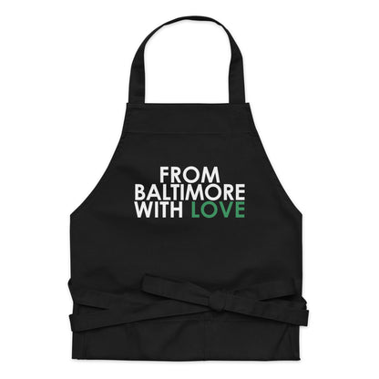 Green cotton apron from Baltimore With Love™ featuring the FBWL logo, shown hanging with adjustable neck strap.