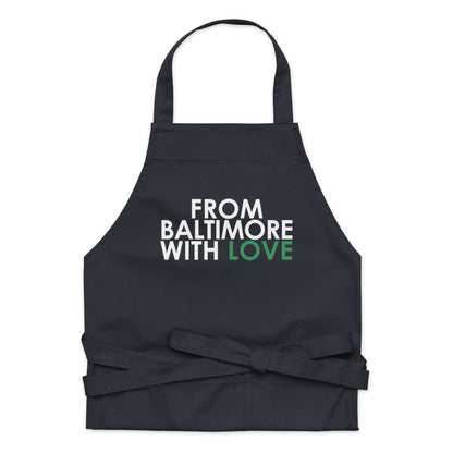 Green cotton apron by From Baltimore With Love™ with adjustable straps, shown hanging on a hook.