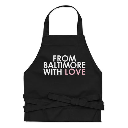 Pink cotton apron by From Baltimore With Love™ with adjustable neck strap and front pockets, ideal for cooking or baking.