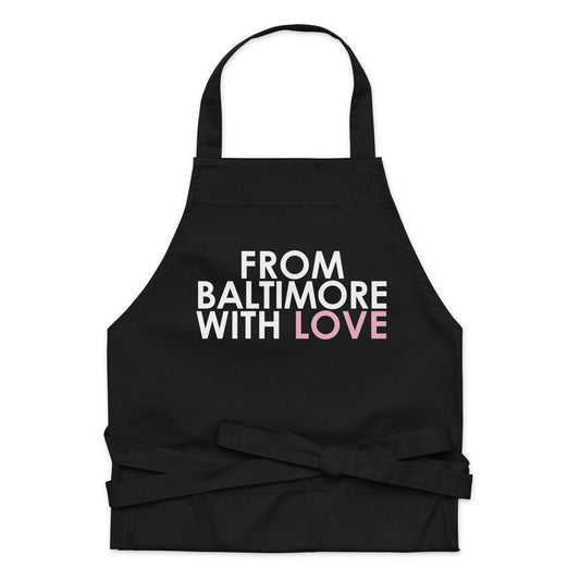 Pink cotton apron by From Baltimore With Love™ with adjustable neck strap and front pockets, ideal for cooking or baking.
